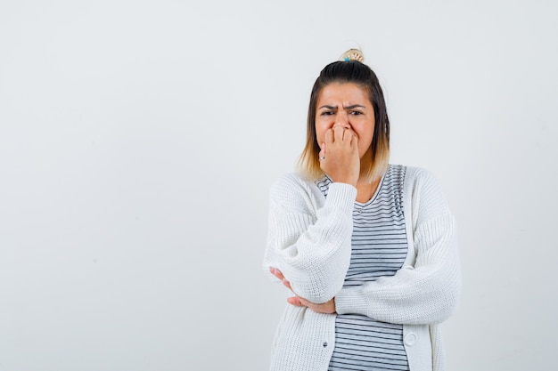 Porträt einer süßen Dame, die emotional Nägel in T-Shirt, Strickjacke beißt und ängstliche Vorderansicht schaut