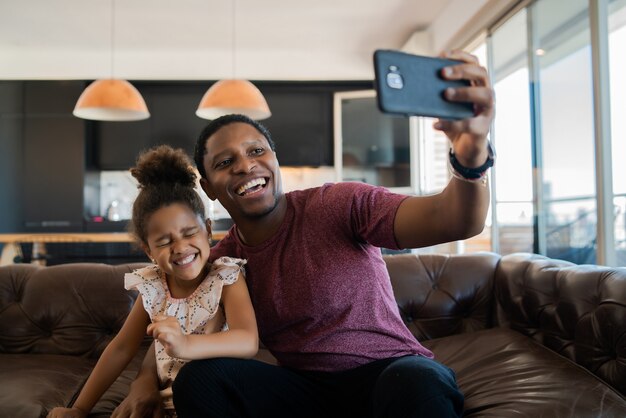 Porträt einer Tochter und eines Vaters, die Spaß zusammen haben und ein Selfie mit Handy zu Hause machen