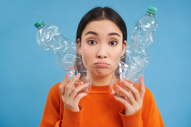 Porträt einer traurigen asiatischen Frau mit Plastikflaschen, verärgert über den Mangel an Recyclingzentren, blauer Hintergrund