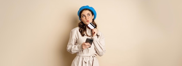 Porträt einer trendigen Frau im Mantel, die ein Smartphone hält, das Kreditkarten-Shopping-Online-Bestellungen zeigt