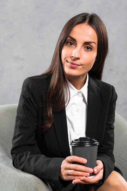 Porträt einer überzeugten jungen Geschäftsfrau, die in der Hand Wegwerfkaffeetasse hält