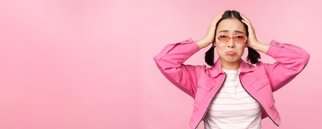Porträt einer unruhigen asiatischen Frau Koreanisches Mädchen hält die Hände auf dem Kopf und schaut in Panik, die verzweifelt und schockiert vor rosafarbenem Hintergrund steht