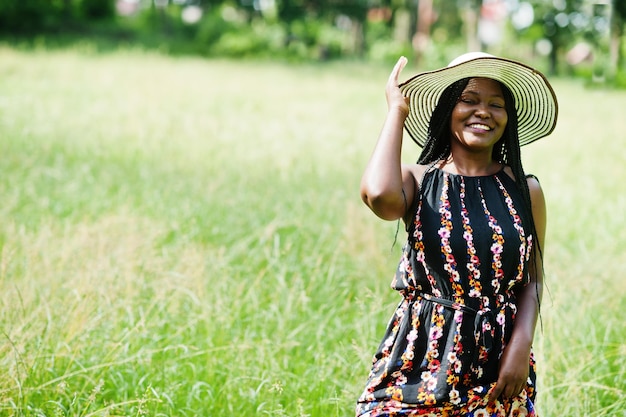Porträt einer wunderschönen afrikanisch-amerikanischen Frau der 20er Jahre mit Sommerhut, die auf grünem Gras im Park posiert