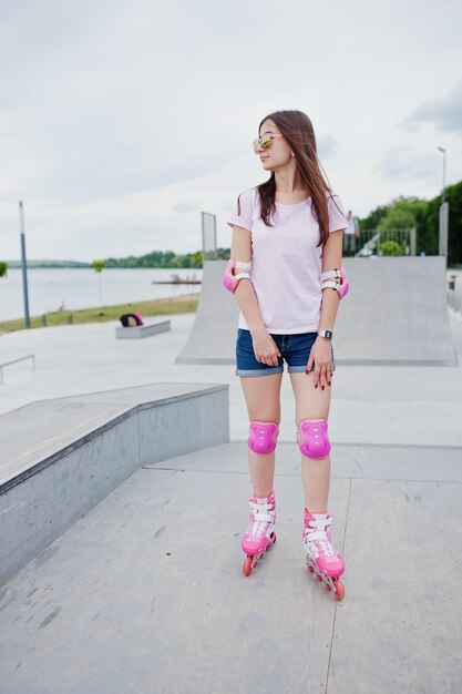 Porträt einer wunderschönen jungen Frau in Shorts, T-Shirt und Sonnenbrille, die im Freien in Rollerblades steht