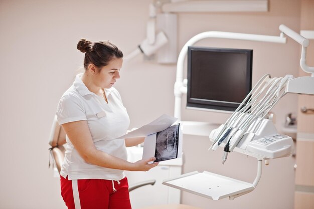 Porträt einer Zahnärztin, die in ihrer Zahnarztpraxis steht und auf Röntgenbilder schaut