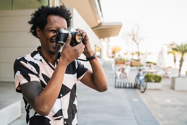 Porträt eines Afro-Mannes, der mit der Kamera fotografiert, während er im Freien auf der Straße spazieren geht