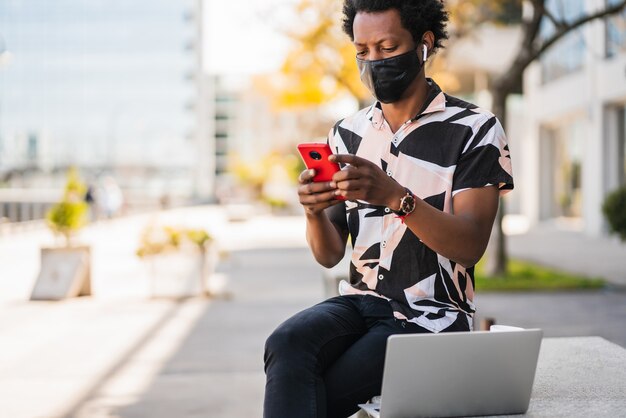 Porträt eines Afro-Mannes, der sein Handy benutzt, während er draußen auf der Straße geht. Neues normales Lifestyle-Konzept.