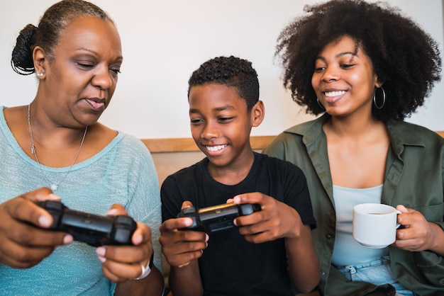 Porträt eines afroamerikanischen Kindes, das Großmutter und Mutter beibringt, wie man Joystick benutzt, um Videospiele zu spielen