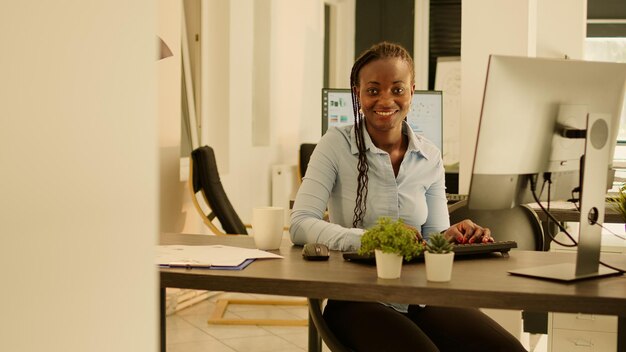 Porträt eines afroamerikanischen Mitarbeiters, der am Geschäftsbericht arbeitet und den Computer am Schreibtisch verwendet. Während des Sonnenuntergangs Notizen machen und E-Mails senden, Brainstorming-Ideen beim Startjob.