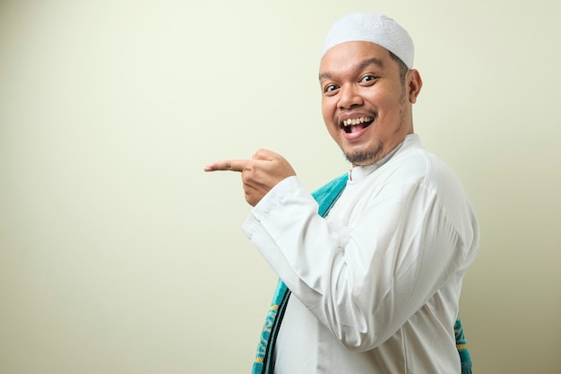 Porträt eines asiatischen jungen muslimischen mannes, der lächelt und darauf zeigt, etwas auf seiner seite zu präsentieren?