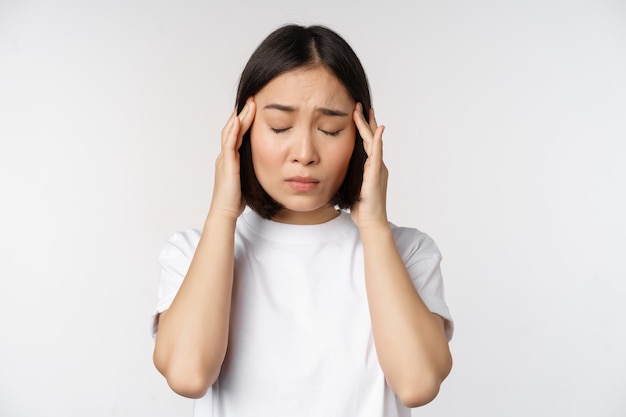 Porträt eines asiatischen Mädchens, das Kopfschmerzen, Migräne oder Kranksein im weißen T-Shirt auf weißem Hintergrund verspürt