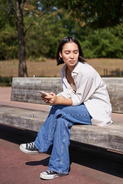 Porträt eines asiatischen Mädchens, das mit dem Smartphone sitzt und traurig aussieht, düster und frustriert wartet