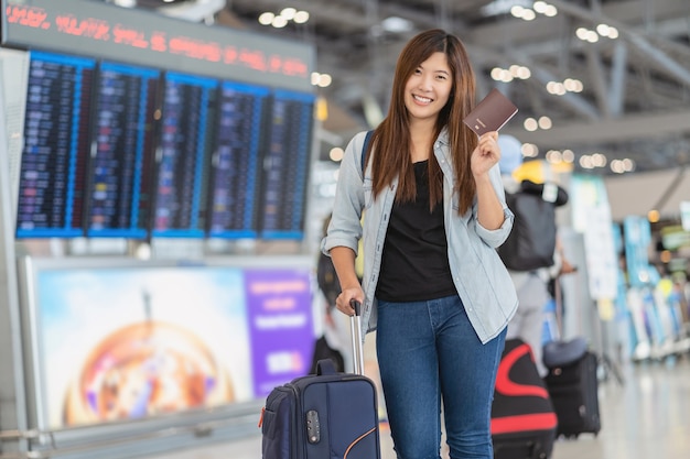 Porträt eines asiatischen reisenden mit gepäck mit reisepass, der über dem flugbrett steht