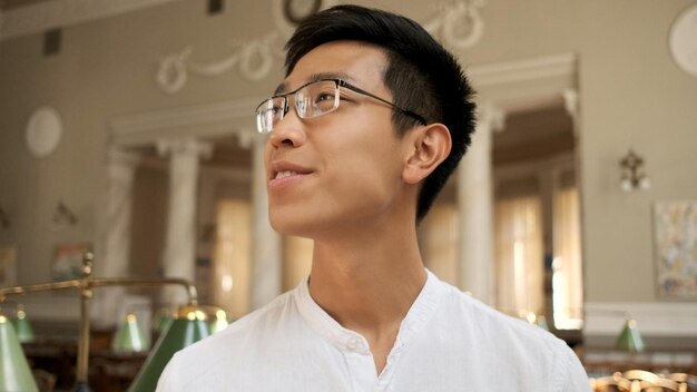 Porträt eines attraktiven asiatischen Studenten mit Brille, der in der Universitätsbibliothek studiert
