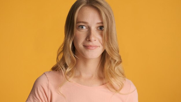 Porträt eines attraktiven blonden Mädchens, das vor der Kamera auf gelbem Hintergrund posiert