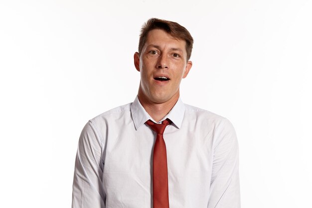 Porträt eines attraktiven brünetten Mannes mit braunen Augen, der ein weißes Hemd und eine rote Krawatte trägt. Er sieht verwundert aus, während er in einem Studio posiert, das über einem weißen Hintergrund isoliert ist. Konzept der Gestik