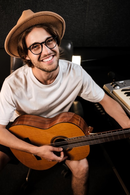 Porträt eines attraktiven, fröhlichen mannes, der glücklich auf einer gitarre spielt und im modernen musikstudio ein neues lied aufnimmt Kostenlose Fotos