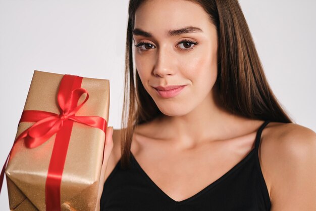 Porträt eines attraktiven lächelnden Mädchens, das eine Geschenkbox hält, die aufmerksam in die Kamera blickt, auf weißem Hintergrund isoliert
