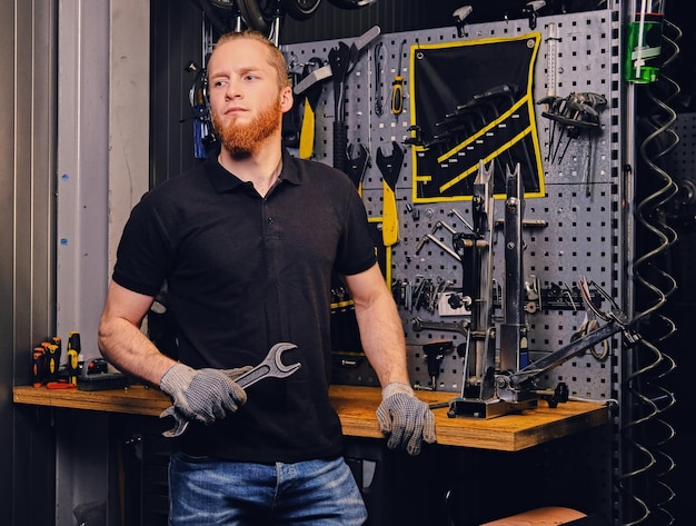 Porträt eines bärtigen Fahrradmechanikers über dem Hintergrund eines Werkzeugständers in einer Werkstatt.
