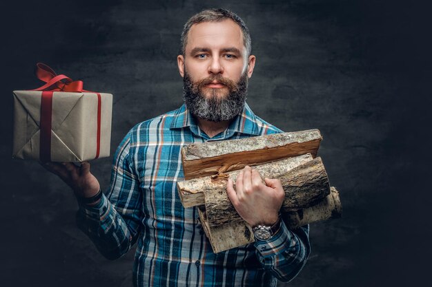 Porträt eines bärtigen Mannes mittleren Alters hält Brennholz und Weihnachtsgeschenkbox.