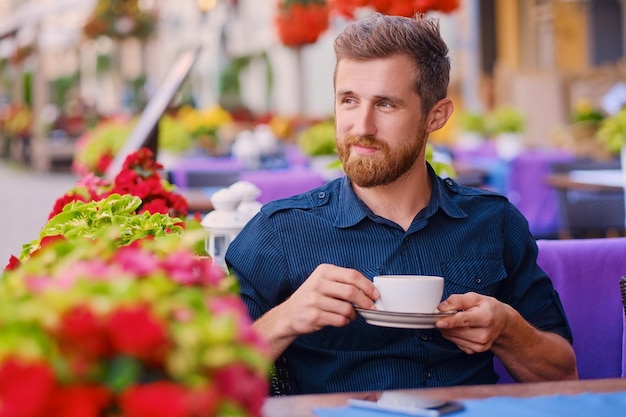 Porträt eines bärtigen rothaarigen Gelegenheitsmannes trinkt Kaffee in einem Café auf einer Straße.