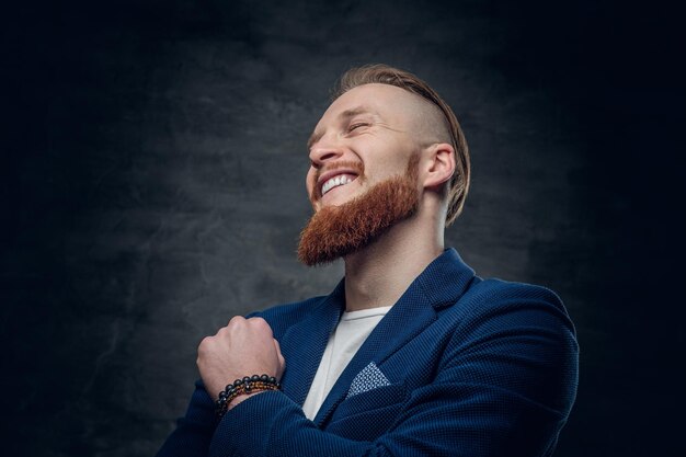 Kostenloses Foto porträt eines bärtigen, rothaarigen hipster-männchens, gekleidet in eine blaue jacke auf grauem hintergrund.