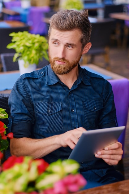 Porträt eines bärtigen rothaarigen Mannes mit einem Tablet-PC am Tisch.