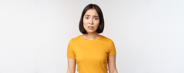 Porträt eines besorgten koreanischen Mädchens, das besorgt in die Kamera schaut, die im gelben T-Shirt vor weißem Hintergrund steht