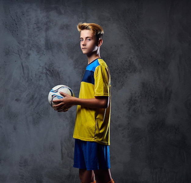 Porträt eines blonden Teenagers, Fußballspieler in gelber Uniform hält einen Ball.