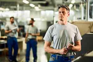 Kostenloses Foto porträt eines cnc-bedieners im mittleren erwachsenenalter, der wegschaut, während er in einer fabrik steht