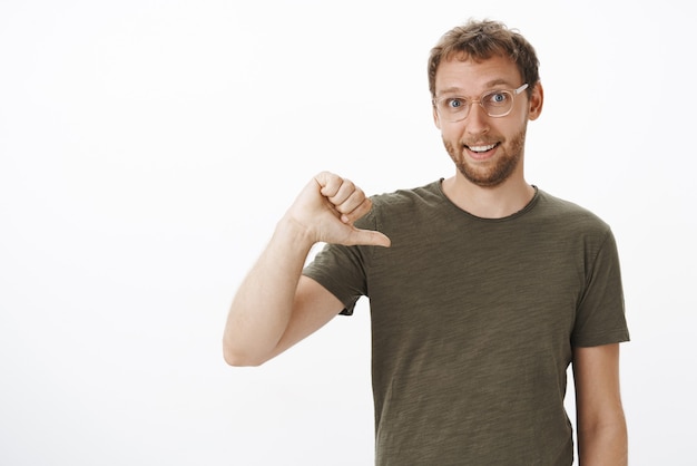 Kostenloses Foto porträt eines ehrgeizigen gutaussehenden männlichen mitarbeiters im dunkelgrünen t-shirt, das auf sich zeigt, während er sich freiwillig bereit erklärt, freudig lächelnder kandidat zu sein