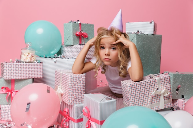 Porträt eines enttäuschten kleinen Mädchens in einem Geburtstagshut