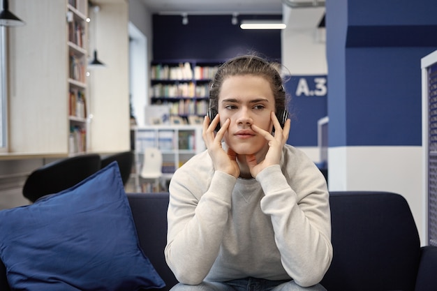 Porträt eines ernsthaften Universitätsstudenten in Freizeitkleidung, der zu Hause Hausaufgaben macht und Verständnisübungen mit modernen drahtlosen Kopfhörern hört