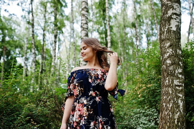 Porträt eines fabelhaften jungen Mädchens in hübschem Kleid mit stilvoller lockiger Frisur, das im Wald oder Park posiert