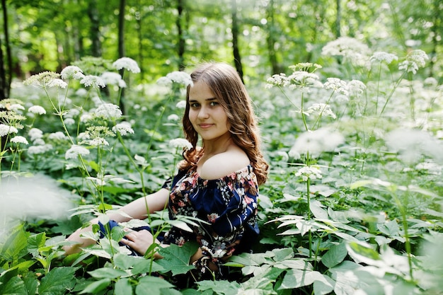 Kostenloses Foto porträt eines fabelhaften jungen mädchens in hübschem kleid mit stilvoller lockiger frisur, das im wald oder park posiert