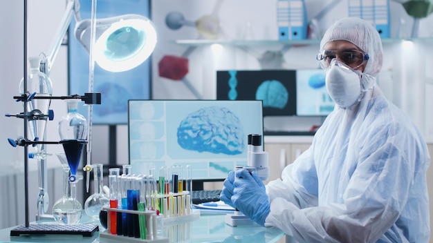 Porträt eines Facharztes mit PPE-Ausrüstung, der die DNA-Probe analysiert, die während des mikrobiologischen Experiments im medizinischen Krankenhauslabor an der Krankheitsdiagnose arbeitet. Medizinkonzept