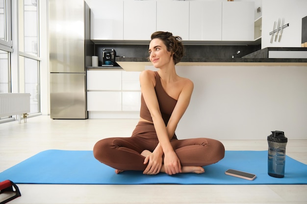 Porträt eines Fitness-Mädchens, das zu Hause in der Küche auf einer Gummimatte Yoga macht und Sportbekleidung trägt