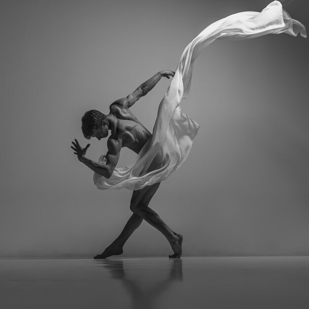 Porträt eines flexiblen, attraktiven Mann-Balletttänzers, der mit einem Stofftuch auftritt, das auf grauem Studiohintergrund isoliert ist