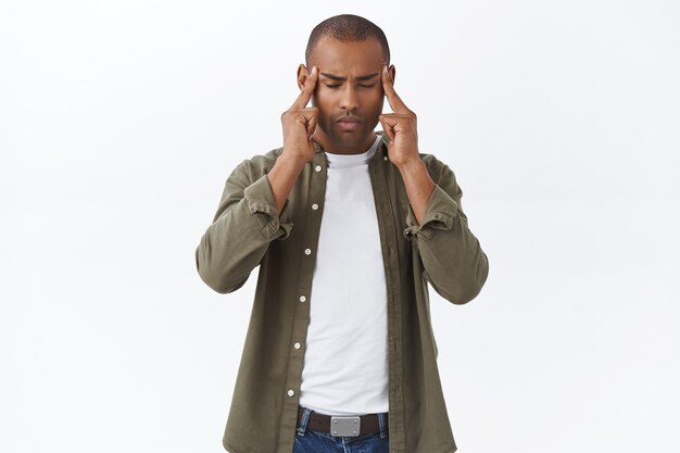 Porträt eines fokussierten, afroamerikanischen Mannes, der Stress verspürt, versucht, sich zu beruhigen und geduldig zu sein, Schläfen zu massieren, Augen zu schließen