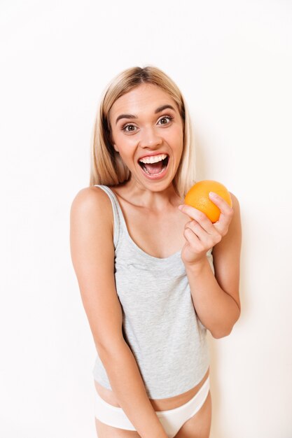 Porträt eines freudigen Mädchens in der Unterwäsche, die orange Frucht hält