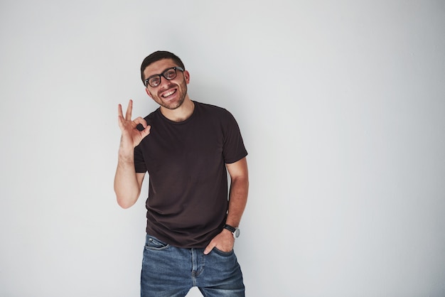 Porträt eines freudigen Mannes im T-Shirt und in den Brillen und zeigt ok Zeichen