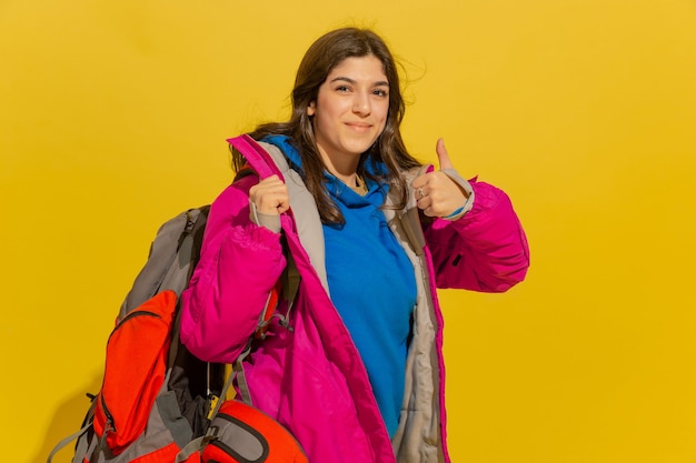 Porträt eines fröhlichen jungen Touristenmädchens mit Tasche und Fernglas lokalisiert auf gelber Studiowand