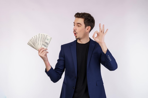 Porträt eines fröhlichen Mannes, der ein Ok-Zeichen zeigt und Geld auf weißem Hintergrund hält