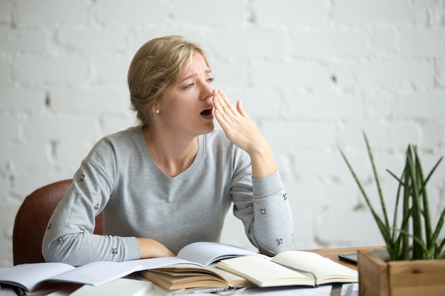 Porträt eines gähnenden Studentenmädchens am Schreibtisch