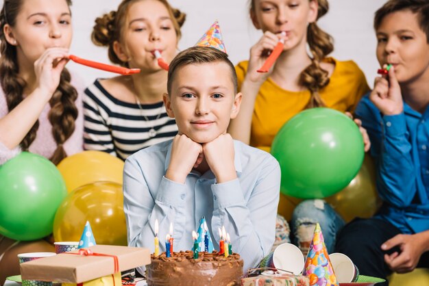 Porträt eines Geburtstagsjungen mit seinen Freunden, die Partyhorn durchbrennen