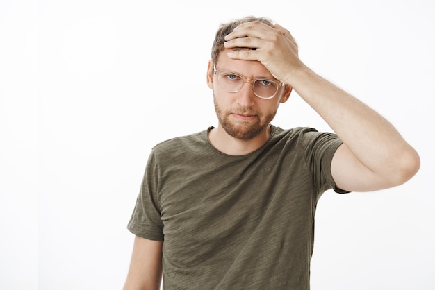 Porträt eines gereizten und verärgerten jungen Geschäftsmannes in Brille und dunkelgrünem T-Shirt, der Hand auf Stirn hält und sauer und wütend Temperament starrt