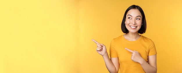 Porträt eines glücklichen asiatischen Mädchens, das mit dem Finger zeigt und nach links lächelt und erstaunt beim Auschecken des Promo-Verbots schaut
