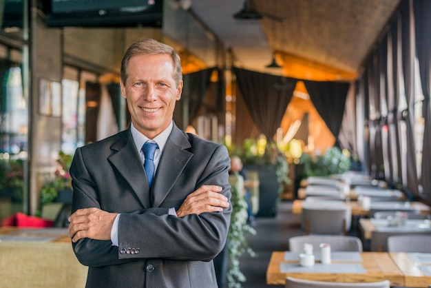 Porträt eines glücklichen erfolgreichen Geschäftsmannes, der im Restaurant mit dem gekreuzten Arm steht