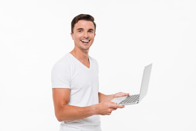 Porträt eines glücklichen freudigen Kerls, der am Laptop arbeitet