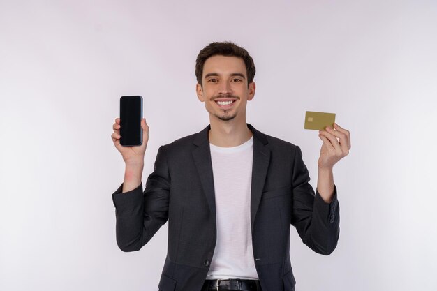 Porträt eines glücklichen jungen Geschäftsmannes, der Handy zeigt und eine Kreditkarte hält, die auf weißem Hintergrundstudio isoliert ist